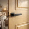 Bold matt black Pina on Square Rosette elegant square internal door handles providing a striking modern contrast on a natural oak wood door.