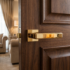 High-end square door handles in a brilliant polished gold finish from the Raflesia collection, mounted on a luxury dark wood paneled door.