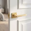 Classic square internal door handles in a soft matt gold finish from the Setia collection, installed on a clean white paneled door.
