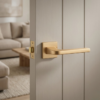 uxury square internal door handles in matt gold, showcasing the Ismena lever design on a square rosette against a softly textured internal door.