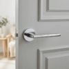 Polished chrome Kalmia on Round Rosette on a grey panelled door, reflecting the sleek round internal door handle design in a bright, minimalist interior.