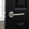 Satin chrome Kalmia on Round Rosette installed on a black door, presenting a sleek round internal door handle in a refined contemporary home environment.