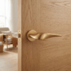 Petunia on Round Rosette in matt gold, featuring sculpted round door handles on a natural oak interior door.