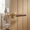 Egeria on Round Rosette in matt gold with brown leather grip, showcasing premium internal door handles on a natural wood door.