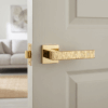 Amarylia on Square Rosette in polished gold, showcasing modern designer door handles with an intricate textured lever on a white interior door.