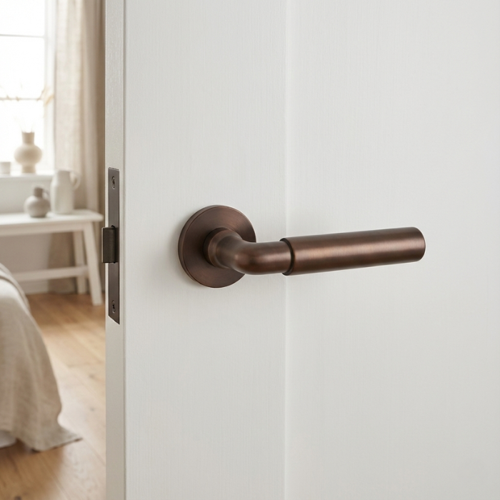 Ficaria - Burnt Umber Ficaria on Round Rosette in burnt umber, showcasing elegant brass door handles with a warm, vintage tone on a white door.