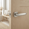 Stella on Rounded Square Rosette in satin nickel, stylish modern round square door handles on a natural light wood door.